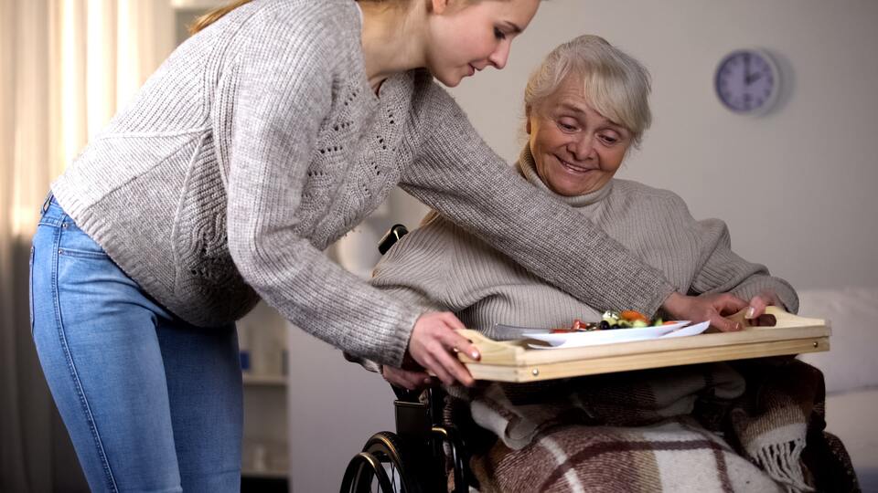 Une jeune femme donnant un plateau repas à une autre femme en fauteuil roulant