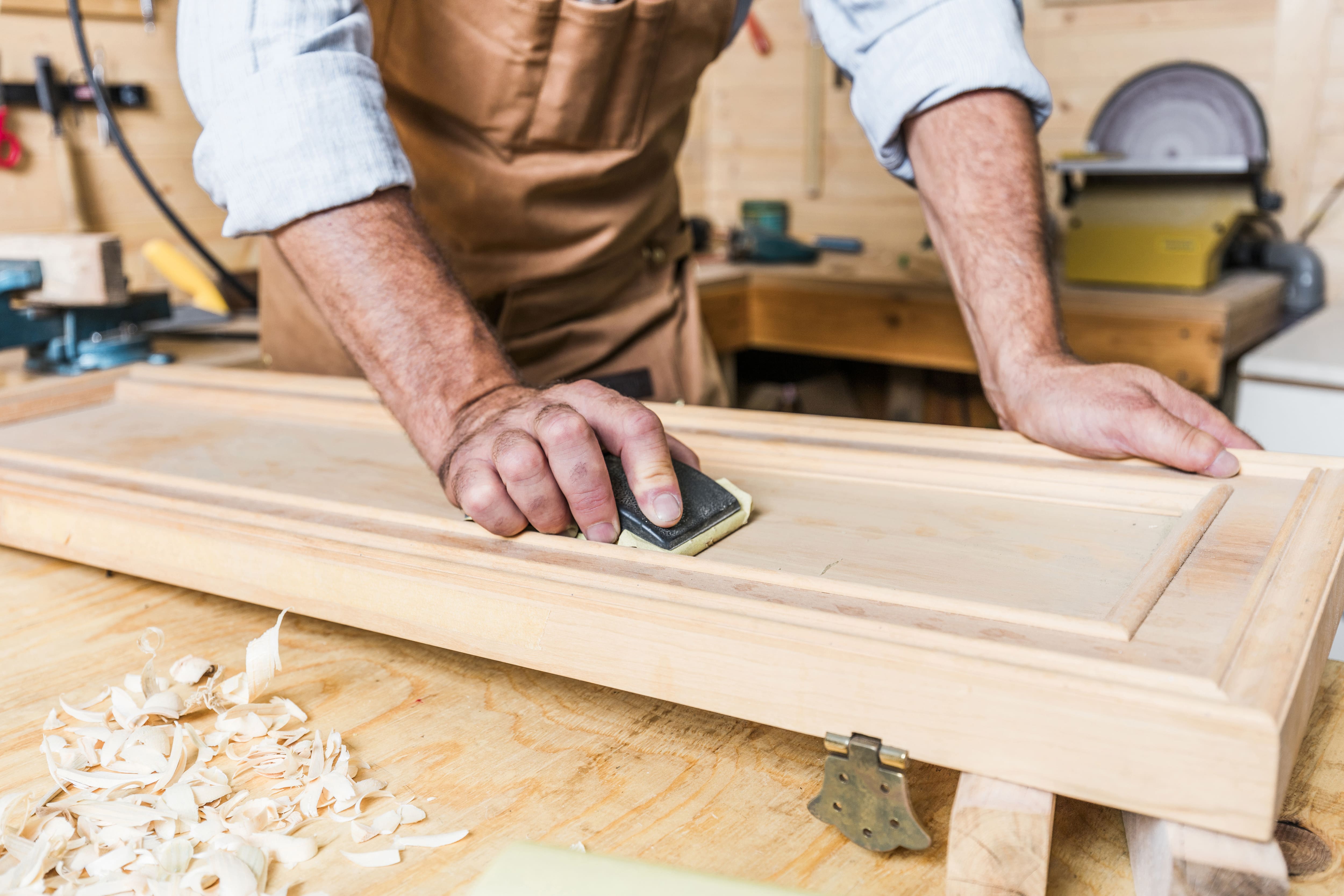 Un menuisier ponce un petite porte en bois